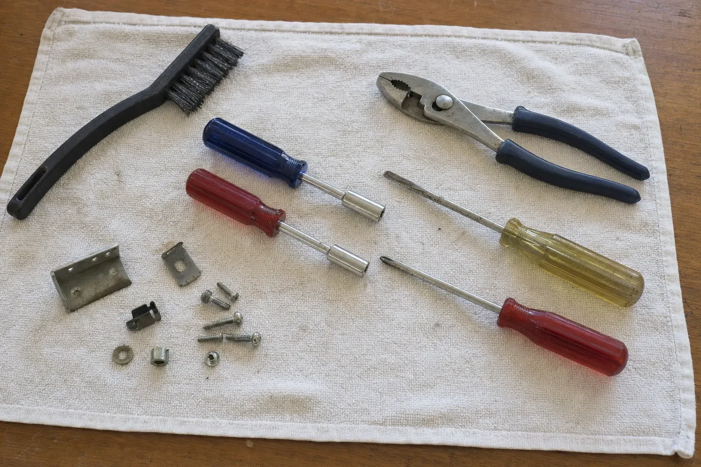Wire brush, pliers, four screwdrivers and a mounting bracket with its screws and clips laid out on a towel
